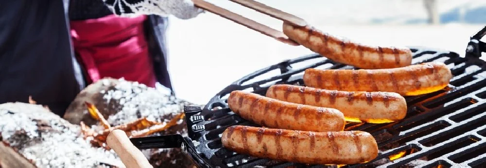 Person grillt Würstchen mit Grillzange